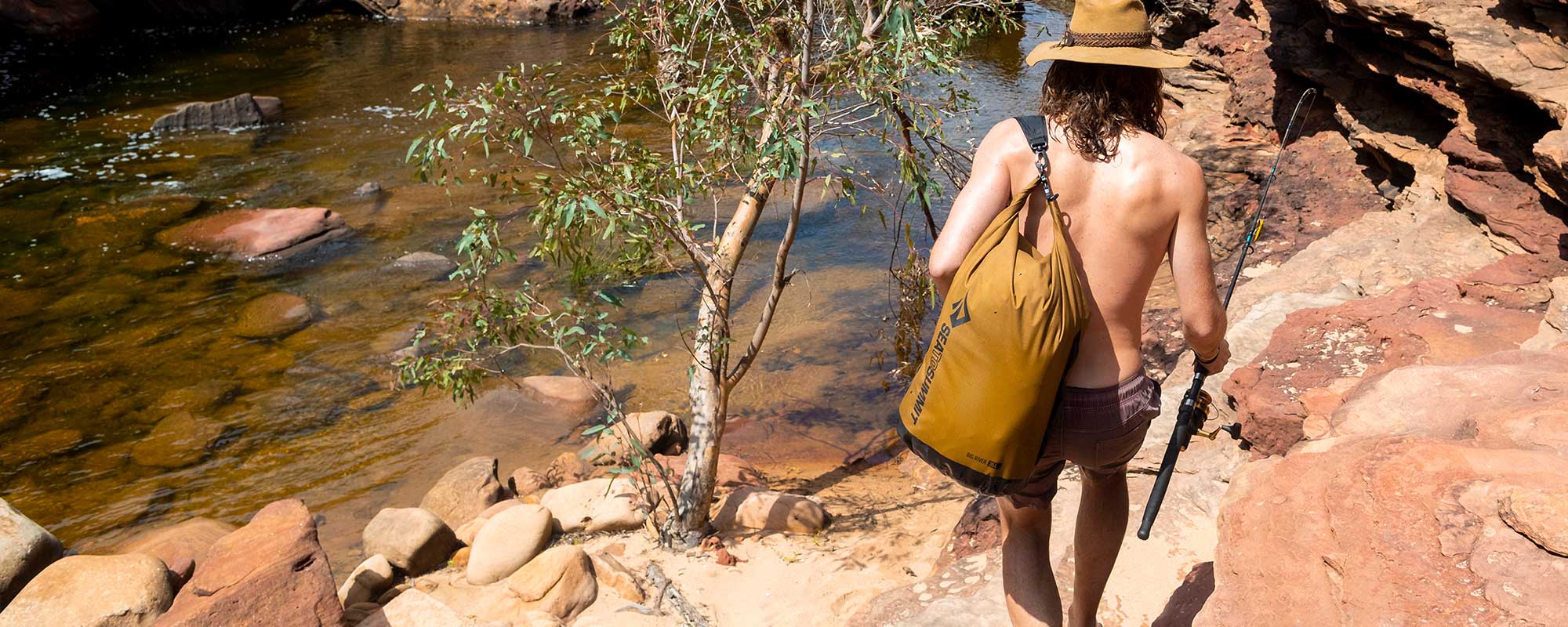 Person hiking near a river with a Big River Dry Bag and Dry Bag Sling