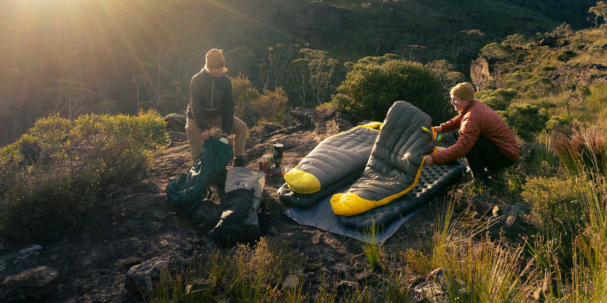 Two people setting up camping gear on a rocky hillside with a scenic background